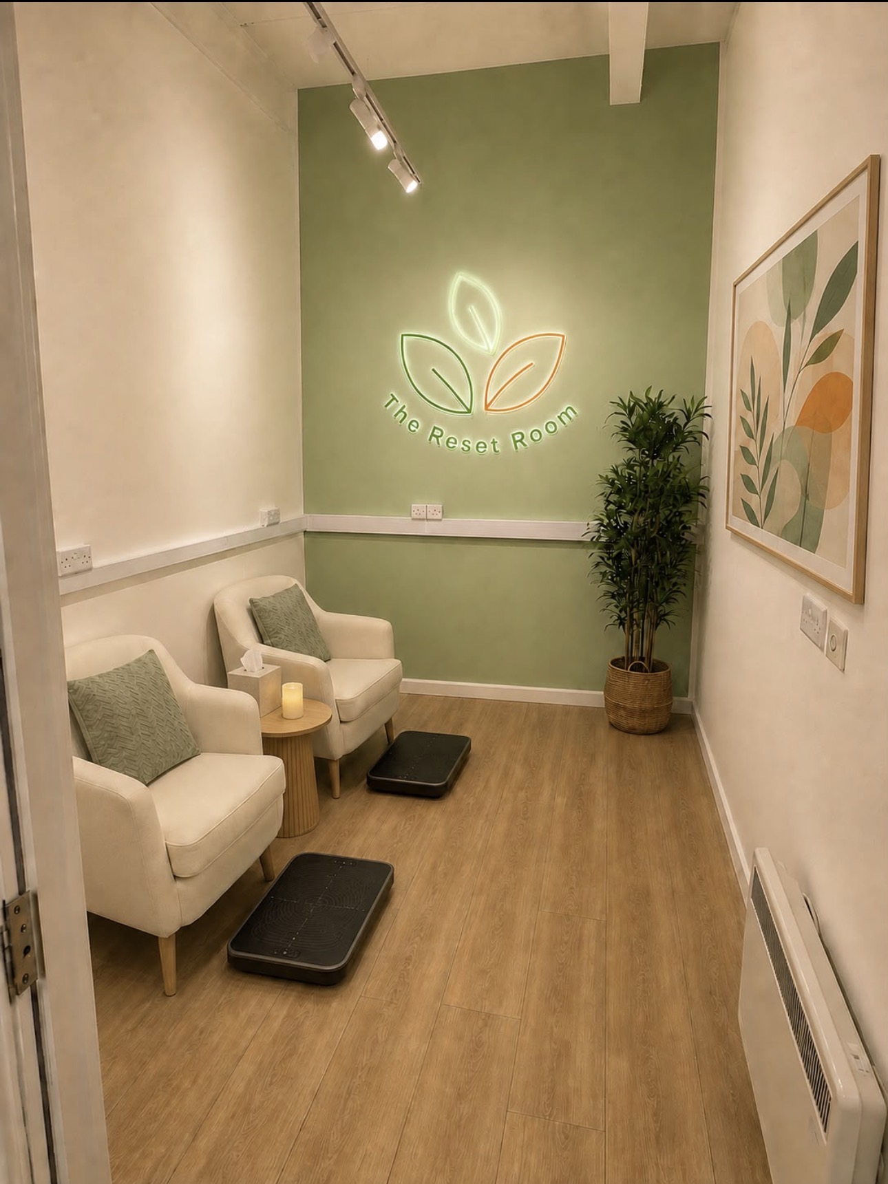 The Reset Room interior with two comfortable armchairs, PEMF foot devices and a neon leaf logo on a sage green wall